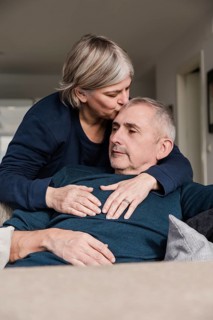 A senior couple shares a tender moment on the couch The woman lovingly kisses the man's head This
