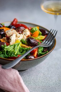 Close-up of a vibrant salad with raw kale leaves, assorted cherry tomatoes, sliced red onions, BBQ