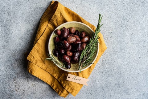 Top view of a ceramic bowl filled with Greek BBQ olives, accented with fresh rosemary sprigs,