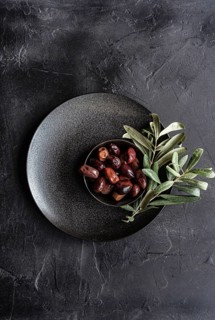 Top view of a dark textured plate filled with glossy Greek BBQ olives garnished with fresh green
