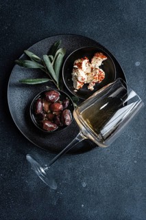 Top view of a sophisticated arrangement featuring Greek BBQ olives in a small black bowl, a portion