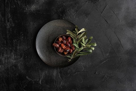Top view of a dark textured plate filled with glossy Greek BBQ olives garnished with fresh green