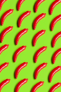 Vibrant, glossy red plastic peppers on a bright green background symbolize artificiality in diet