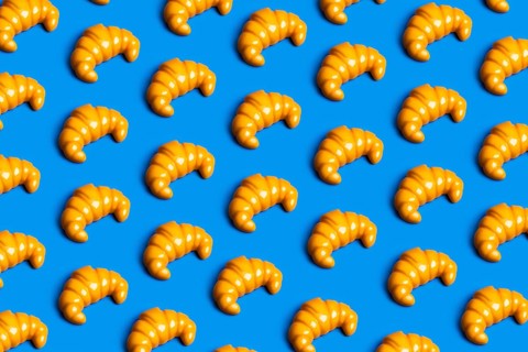 A vibrant pattern of plastic croissants against a blue background, symbolizing the clash between
