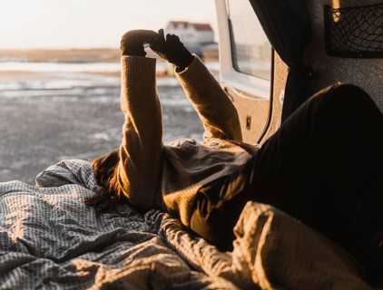 Unrecognizable woman lounging in a van during a camping trip in Iceland. She stretches her arms
