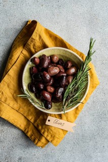 Top view of a ceramic bowl filled with Greek BBQ olives, accented with fresh rosemary sprigs,