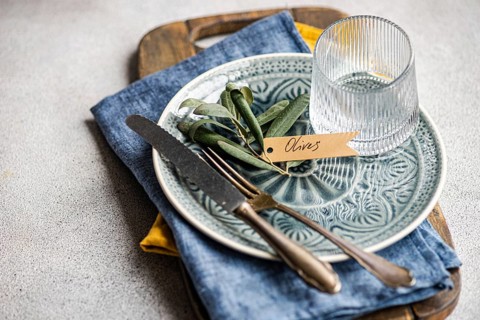 Sophisticated table setting featuring olive leaves on a ceramic plate with a tag, accompanied by a