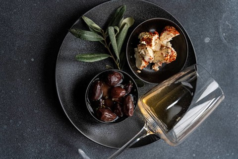 Top view of a sophisticated arrangement featuring Greek BBQ olives in a small black bowl, a portion