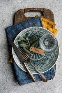 Top view of olive leaves artistically on ornate tableware. A rustic wooden board, vintage cutlery,