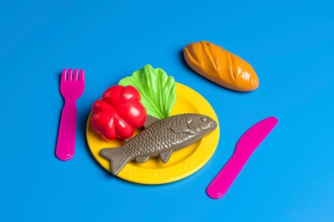 A colorful display with plastic toy food on a plate, including fish, bread, and vegetables,