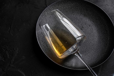 From above, an elegant glass of dry white wine placed carefully on a textured black plate,