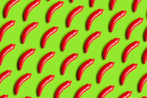 Rows of bright red plastic peppers on a bold green background This image critiques junk food