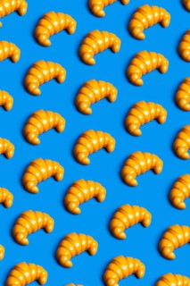 Brightly colored plastic croissants on a vibrant blue background, symbolizing the critique of