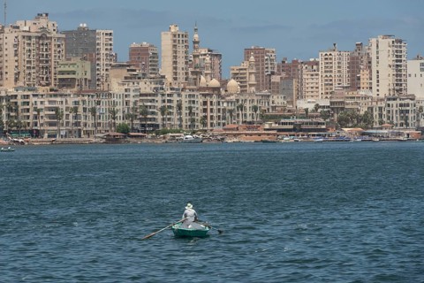 A lone Egyptian fishermen in a small boat fishing in the Mediterranean sea with the skyline of