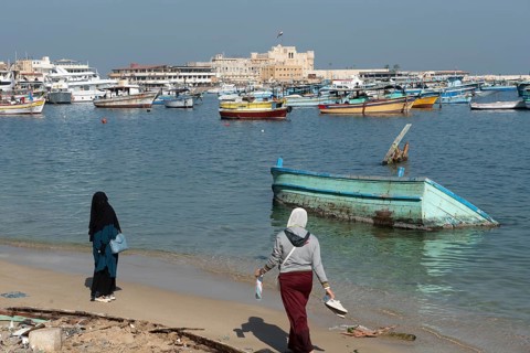 Alexandria, Egypt. December 1st 2022 Two Muslim women walk on the beach near a sunken boat in front