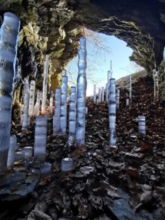 Icicles rise in a brightly lit rock cave with colorful leaves, hiking in the Franconian Forest