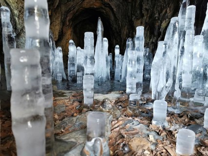 Tall icicles stretch out in a dark cave with stony walls, winter, hiking in the Franconian Forest