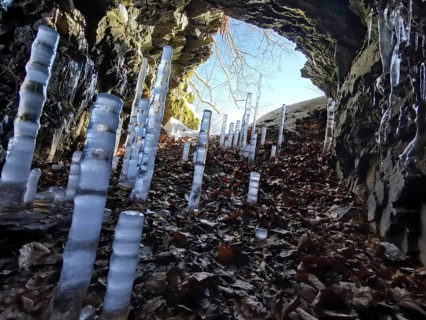 Icicles grow in a rock cave, surrounded by autumn leaves and sunlight, migrate in the Franconian