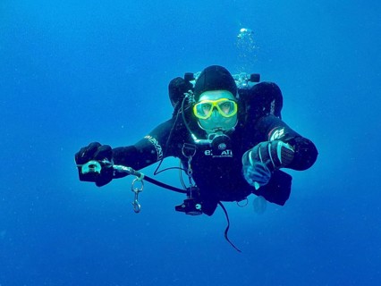 A diver with complete diving equipment extends the second controller to his dive partner, who has
