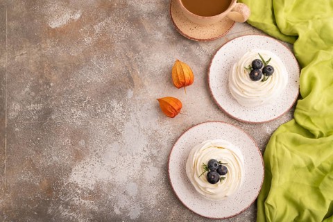 Pavlova Meringue dessert with crisp meringue and blueberry, cup of coffee, on brown concrete
