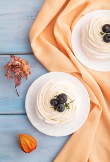 Pavlova Meringue dessert with crisp meringue and blueberry on blue wooden background with orange