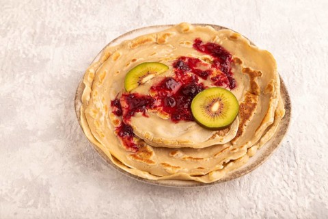 Stack of Plain Fried pancakes with jam and kiwi on gray concrete. side view, close up
