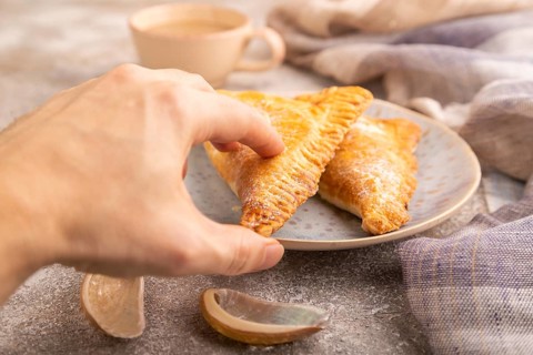 Triangles Pie, Puff Pastry, Samsa with cherry jam on brown concrete background and linen textile