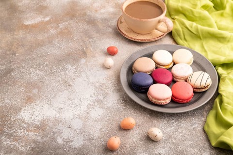 Macarons colourful cookies dessert, cup of coffee, on brown concrete background with green linen