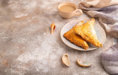 Triangles Pie, Puff Pastry, Samsa with cherry jam on brown concrete background and linen textile,