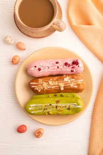 Glazed Eclairs on white wooden background and orange linen textile, cup of coffee, top view, flat
