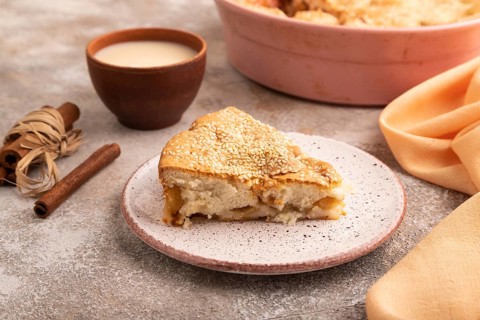 Apple Charlotte cake on brown concrete background and orange linen textile, cup of milk, side view,