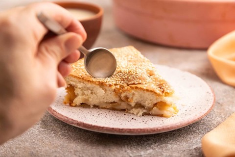 Apple Charlotte cake with hand on brown concrete background and orange linen textile, cup of milk,