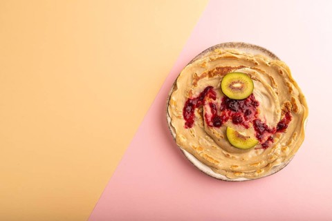 Stack of Plain Fried pancakes with jam and kiwi on pink and orange pastel paper background. top