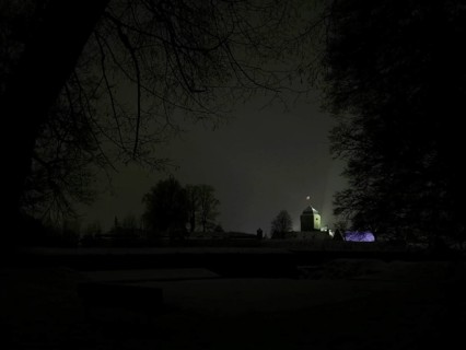 Night view of a dark landscape with a dimly lit, silhouetted Rosenberg Fortress, Kronach,