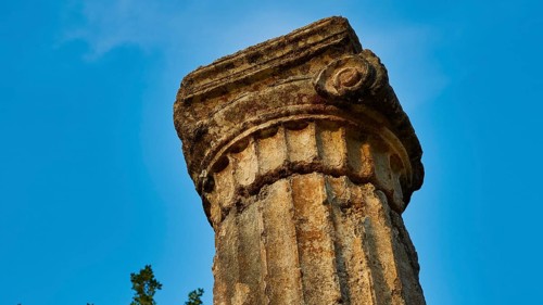 Pillar of Philippeion, head of an ancient stone column with decorated surface against a blue sky,