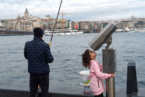Istanbul, Turkey. January 3rd 2025. A man fishing and a child plays with street binoculars beside