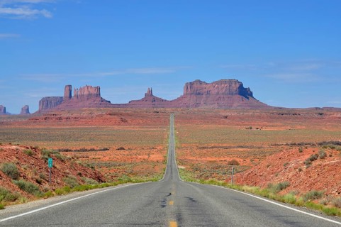 The long, straight road runs through a desert-like landscape with rocks. Access to Monument Valley,