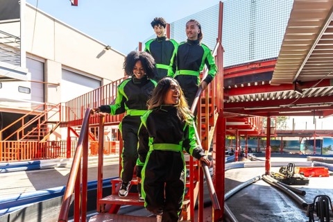 Group of diverse friends wearing racing suits and feeling excited, walking down stairs together at
