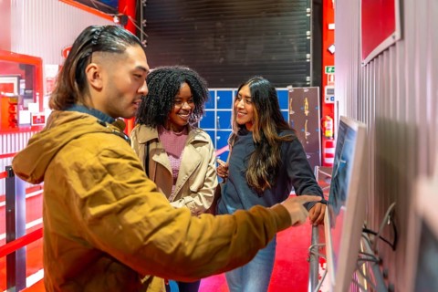 Diverse group of friends smiling and pointing at a touchscreen to select races and book indoor go