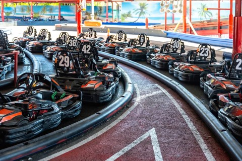 Rows of empty go karts lined up on an indoor race track, engines idle, safety barriers hugging the