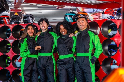 Happy diverse friends smiling, wearing green racing suits, standing together in a karting facility