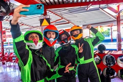 Group of four diverse friends wearing colorful helmets and racing suits, smiling and posing for a