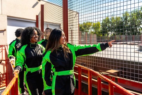 Diverse group of friends in racing suits smiling and pointing at the go kart track, ready for a