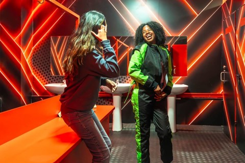 Two friendsone in a racing jumpsuit, the other casuallaugh and bond under vivid red neon in a