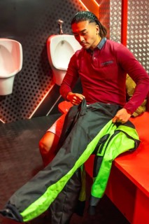 Young man sitting in a changing room, putting on a black and green racing suit for an upcoming
