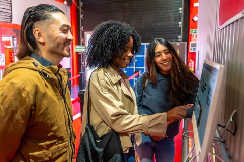Diverse group of young adult friends laughing and talking while interacting with a self service