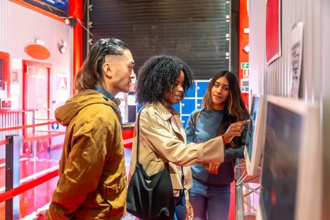 Diverse friends interacting with a digital touchscreen display, selecting racing karts for a fun