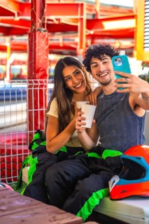 Young couple wearing racing suits taking a selfie during a karting break, showing happiness and