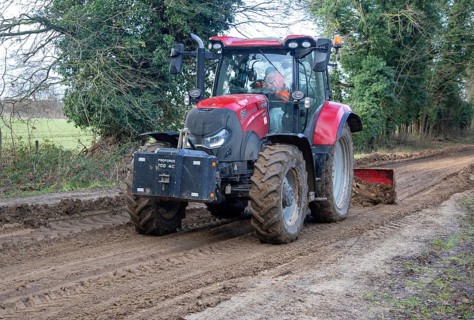Tractor grading and levelling work repair a muddy, flood-prone country lane, Sutton, Suffolk