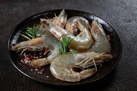 Fresh raw white-footed shrimp, tiger prawns vannamei, on a black plate, with spices and herbs